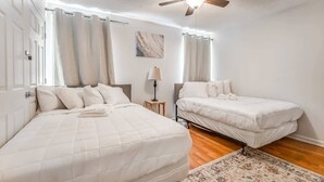 Quarto com duas camas, um ventilador de teto, mesa de cabeceira e janela com cortinas.