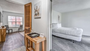 A hotel room with a bed, a wooden side table with a tray, a chair, and a painting on the wall. - Tulip Tree Cottage (Memphis)