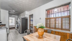 A compact kitchen with modern appliances, a dining area with a wooden table, and a window with wooden shutters. - Tulip Tree Cottage (Memphis)
