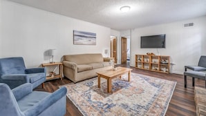 A living room with a sofa, armchairs, a coffee table, a TV, and a bookshelf. - Tulip Tree Cottage (Memphis)