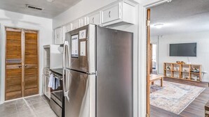 A modern kitchen with stainless steel appliances, wooden cabinets, and a large TV in the adjacent living area. - Tulip Tree Cottage (Memphis)