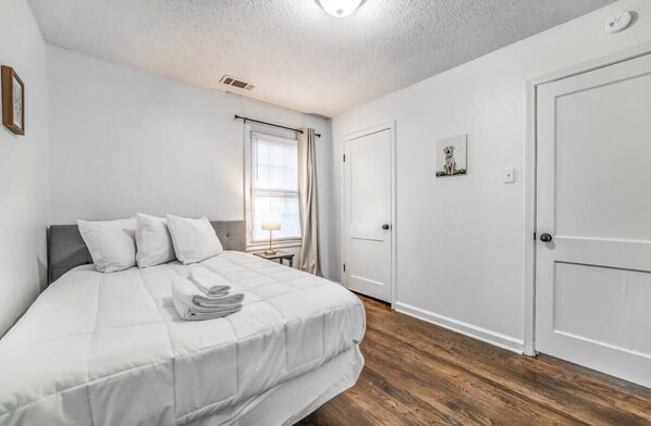A bedroom with a bed, a window with curtains, a door, and a small table with a lamp. - Parnassus Cottage (Memphis)