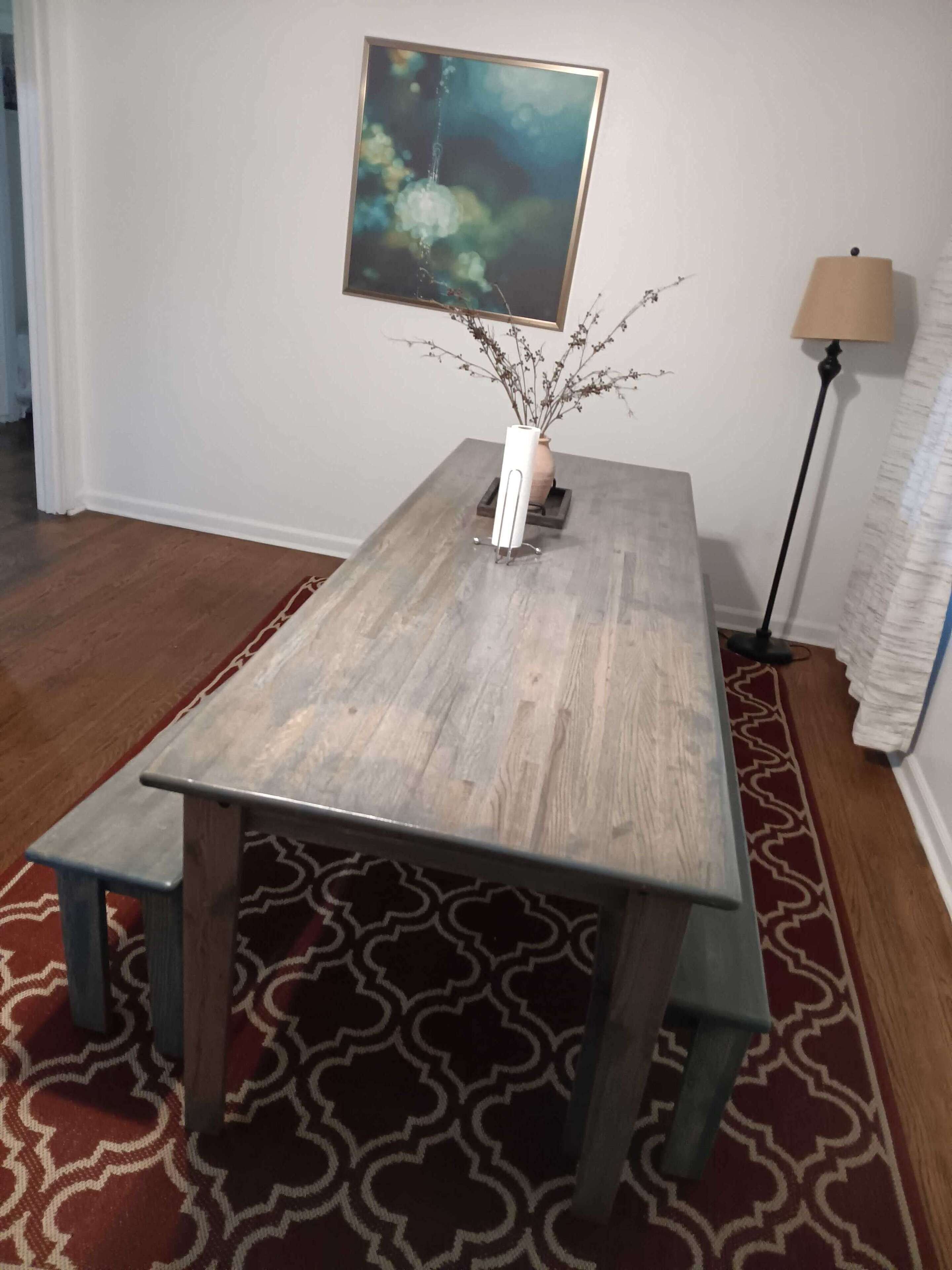 Ein Esstisch mit einer Blumenvase, einem Bild an der Wand und einer Stehlampe.