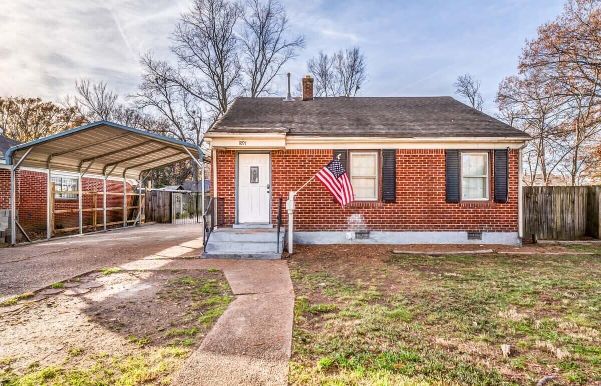 A single-story brick house with a covered porch, a front door, and an American flag.