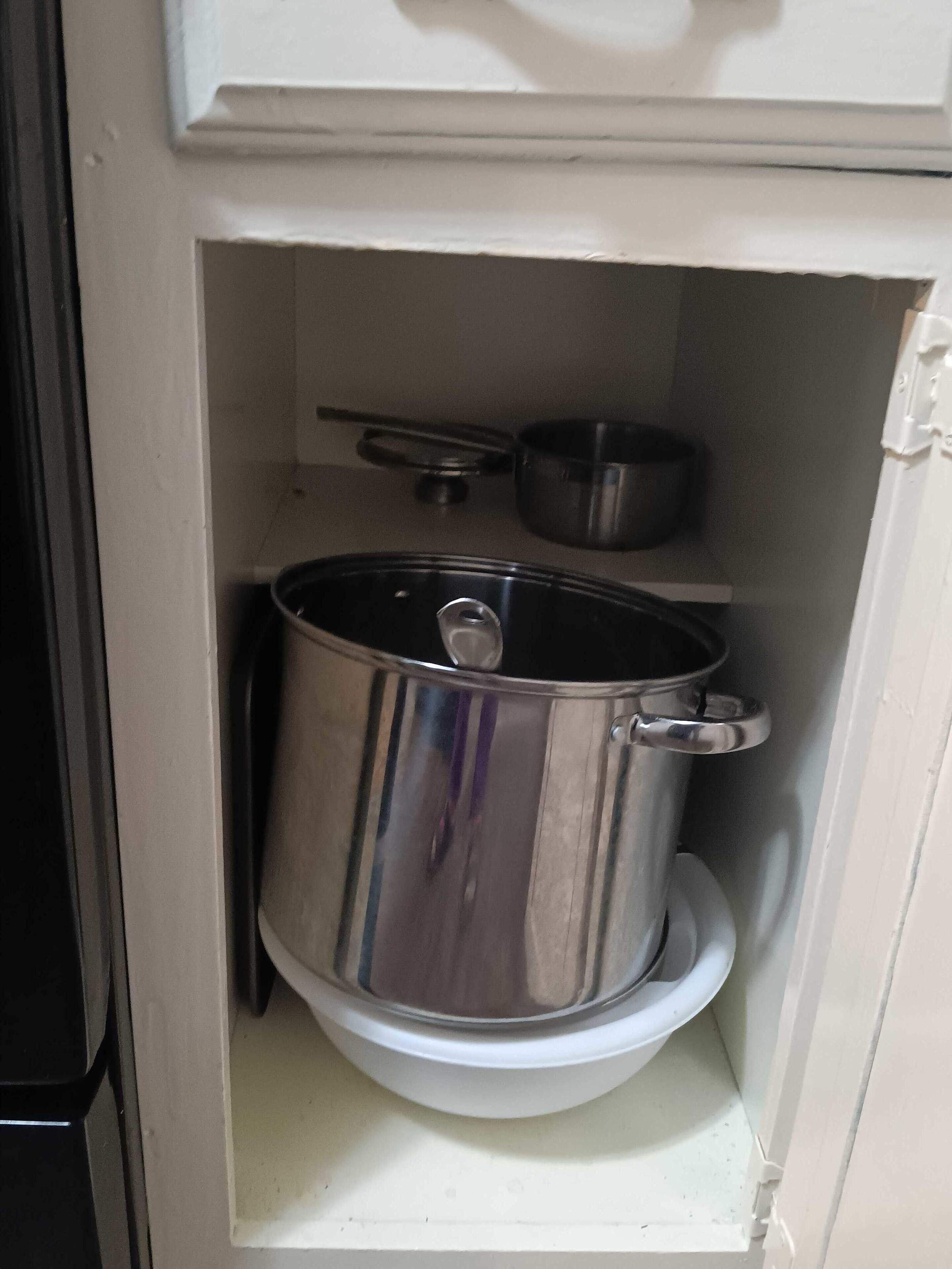 Ett kompakt kök med en kastrull i rostfritt stål på en vit bänkskiva.