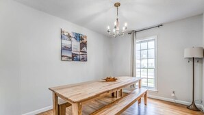 A dining area with a wooden table and bench, a chandelier, a window, and a floor lamp. - Judy Lynn Collective (Memphis)