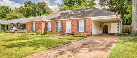 A single-story brick house with a covered porch, a driveway, and a lawn.