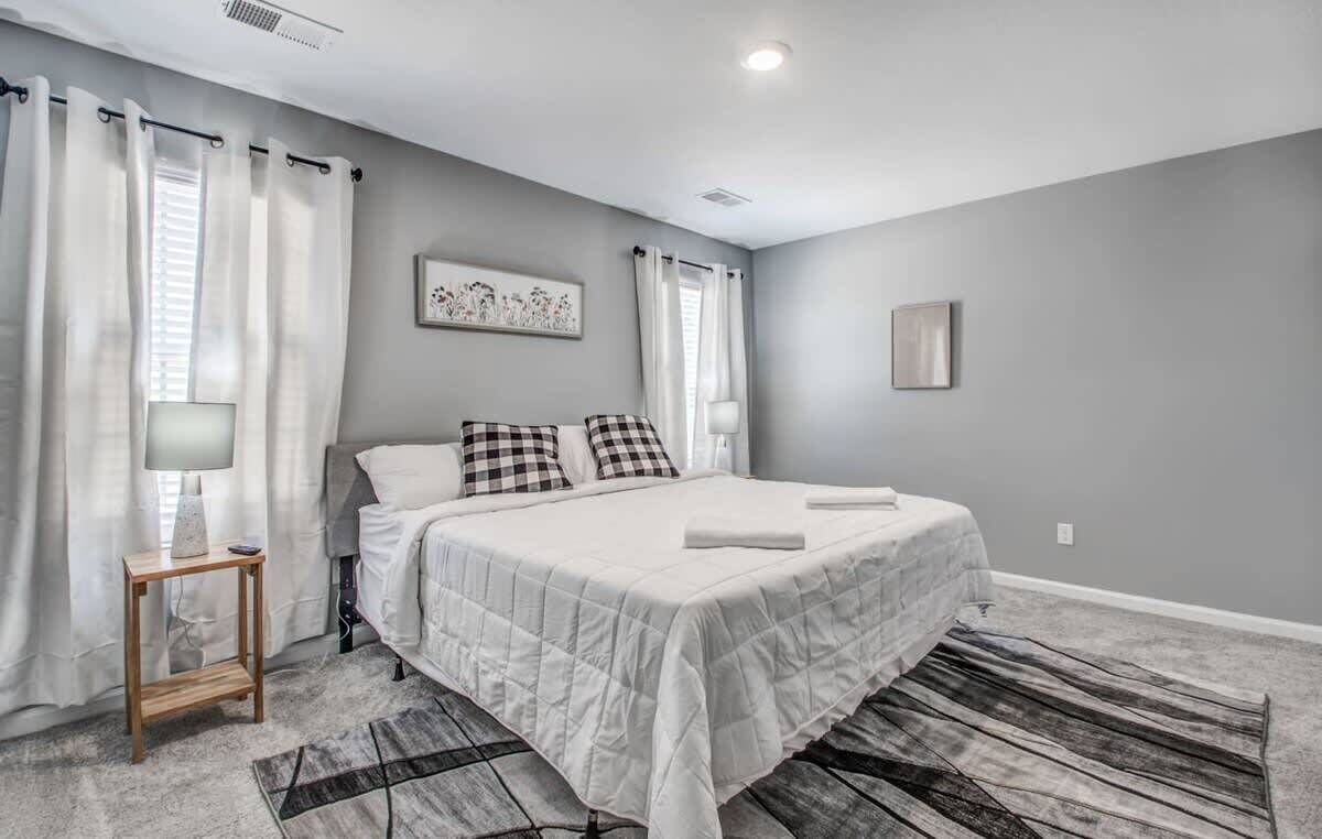 A bedroom with a bed, a bedside table, a lamp, a rug, and a wall art piece.