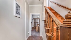 A hallway with a brick floor leading to a wooden staircase with a banister. - Pomona Cottage (Memphis)
