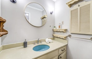 A bathroom with a round mirror, a blue sink, a towel rack, and a shelf with toiletries. - Pomona Cottage (Memphis)