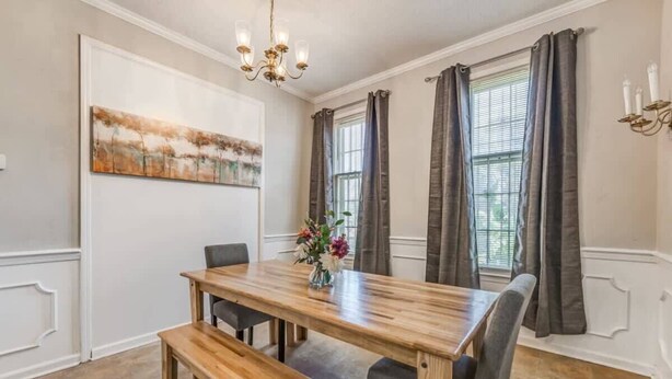 A dining room with a wooden table, benches, and chairs. There is a chandelier, a painting on the wall, and a window with curtains. - Pomona Cottage (Memphis)