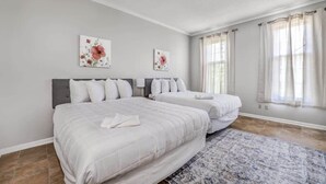A bedroom with two beds, a patterned rug, and floral artwork on the walls. - Pomona Cottage (Memphis)