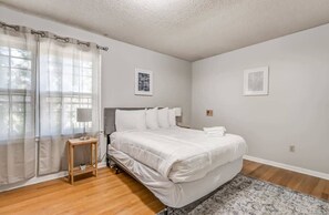 A bedroom with a bed, a small table, a window with sheer curtains, and a wall-mounted air vent. - Pomona Cottage (Memphis)