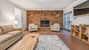 A living room with a brick fireplace, two armchairs, a sofa, a coffee table, and a TV on the wall. - Pomona Cottage (Memphis)