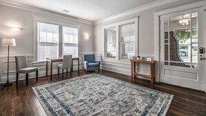 A spacious room with hardwood flooring, a large patterned rug, a blue armchair, a small table, and a door with a glass panel. - Parkway Nest (Memphis)