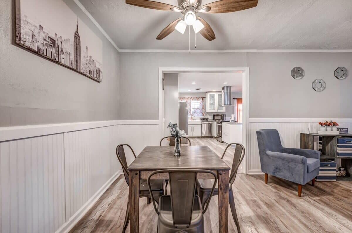 A dining area with a wooden table and chairs, a ceiling fan, and a cityscape artwork on the wall.