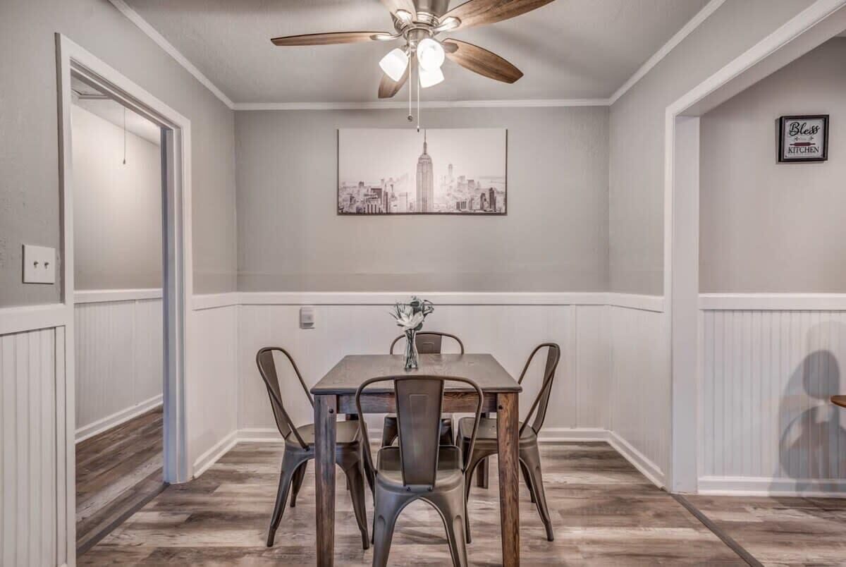 Un coin repas avec une table et des chaises, un ventilateur de plafond et un tableau représentant un paysage urbain accroché au mur.
