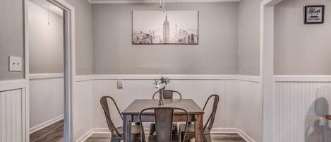 Un coin repas avec une table et des chaises, un ventilateur de plafond et un tableau représentant un paysage urbain accroché au mur.