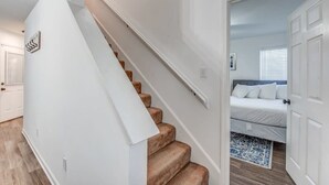 Una escalera que lleva a un dormitorio con una cama, una puerta y una lámpara fijada a la pared.