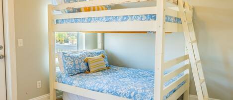 A bunk bed with floral bedding, a window with blinds, and a wooden ladder.