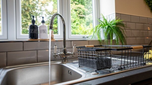 A kitchen with a stainless steel sink, a faucet, and a dish rack. There are two bottles labeled "DISHES" and "HANDS" on the windowsill. - Luxury 5BR Home | Hot Tub | EV-Friendly Stay (West Bromwich)