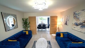A modern living room with two blue sofas, a white marble coffee table, and a dining area in the background. - Luxury 5BR Home | Hot Tub | EV-Friendly Stay (West Bromwich)