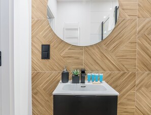 A modern bathroom with a large mirror, wooden wall tiles, a black sink, and a small potted plant. - Wilson Park Serene Studio #4 (Poznań)