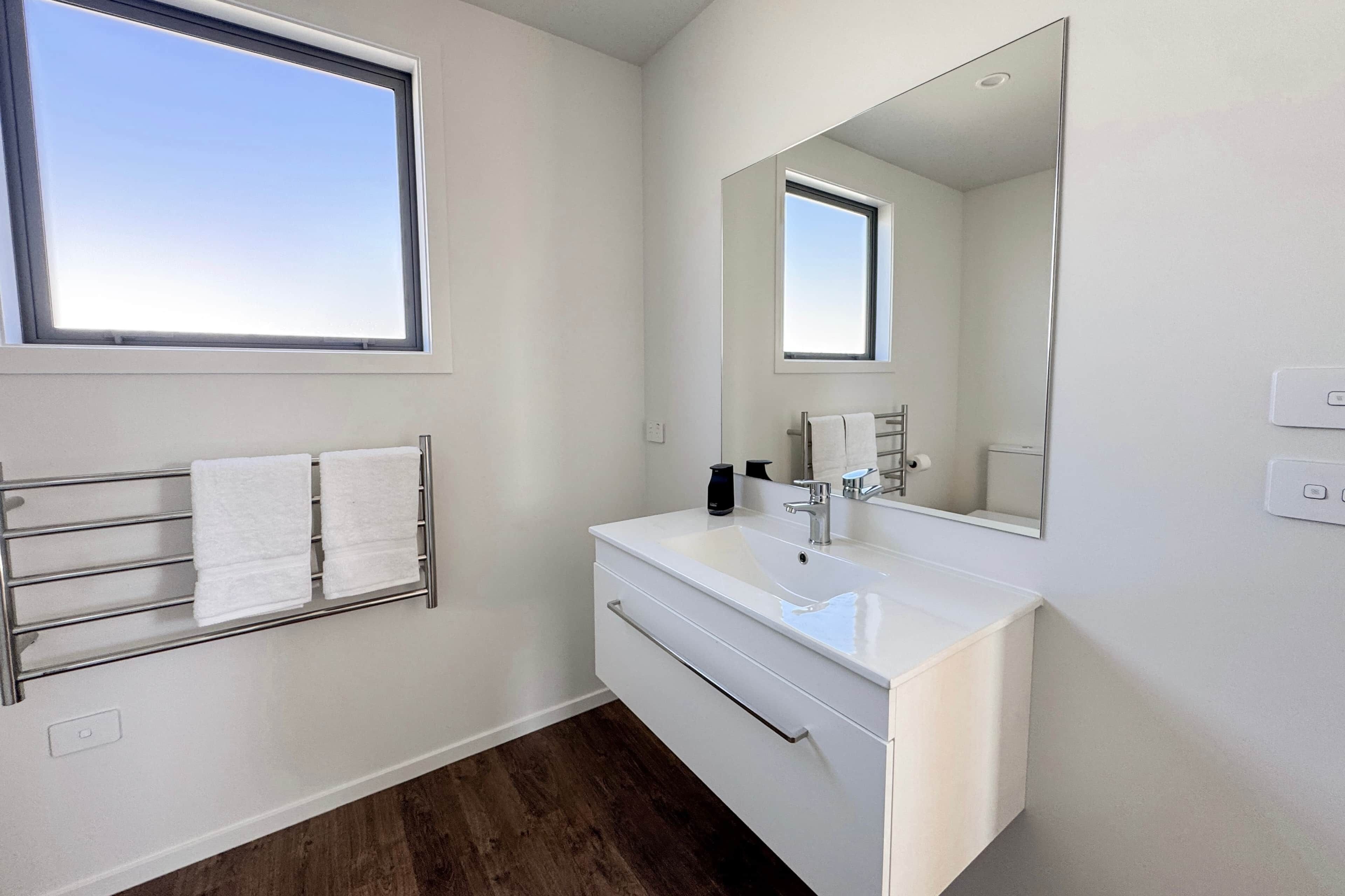 A modern bathroom with a white vanity, a large mirror, and a towel rack.