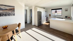A modern kitchen with a stainless steel refrigerator, a dining area with a wooden table and chairs, and a large window providing natural light. - Roto Cottage - Lake Tekapo (Lake Tekapo)