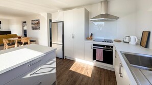 A modern kitchen with white cabinetry, a stainless steel range hood, and a built-in oven. - Roto Cottage - Lake Tekapo (Lake Tekapo)