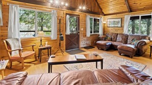A cozy cabin interior with wooden walls, a leather sofa, a rocking chair, and a dining table.