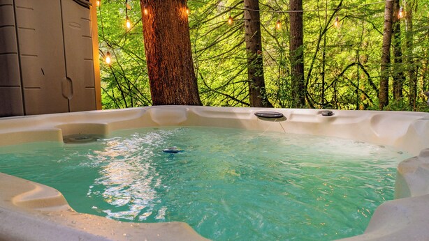 A hot tub with a clear blue water surface, surrounded by trees and a wooden structure.