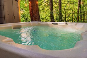 A hot tub with a clear blue water surface, surrounded by trees and a wooden structure.