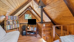 A cozy attic bedroom with a sloped ceiling, wooden bookshelves, a flat-screen TV, a fireplace, and a bed.