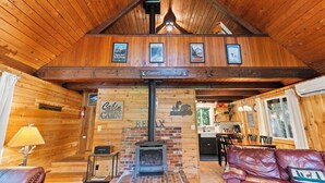 A cabin interior with a wooden ceiling, a brick fireplace, a dining area, and a cozy seating area.