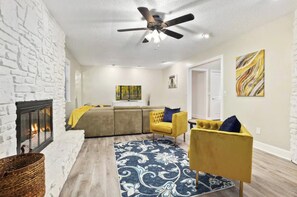 A living room with a fireplace, a ceiling fan, a sofa set, and a patterned rug. - NWA Getaway Pool, Arcade, Trails (Springdale)