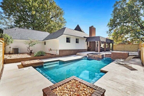 A backyard with a swimming pool, a covered patio, and a brick fire pit. - 4BR Game Room House – 20 Min to Razorback Stadium (Springdale)