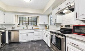 A kitchen with white cabinets, a stainless steel dishwasher, a stove, and a microwave. - NWA Getaway Pool, Arcade, Trails (Springdale)