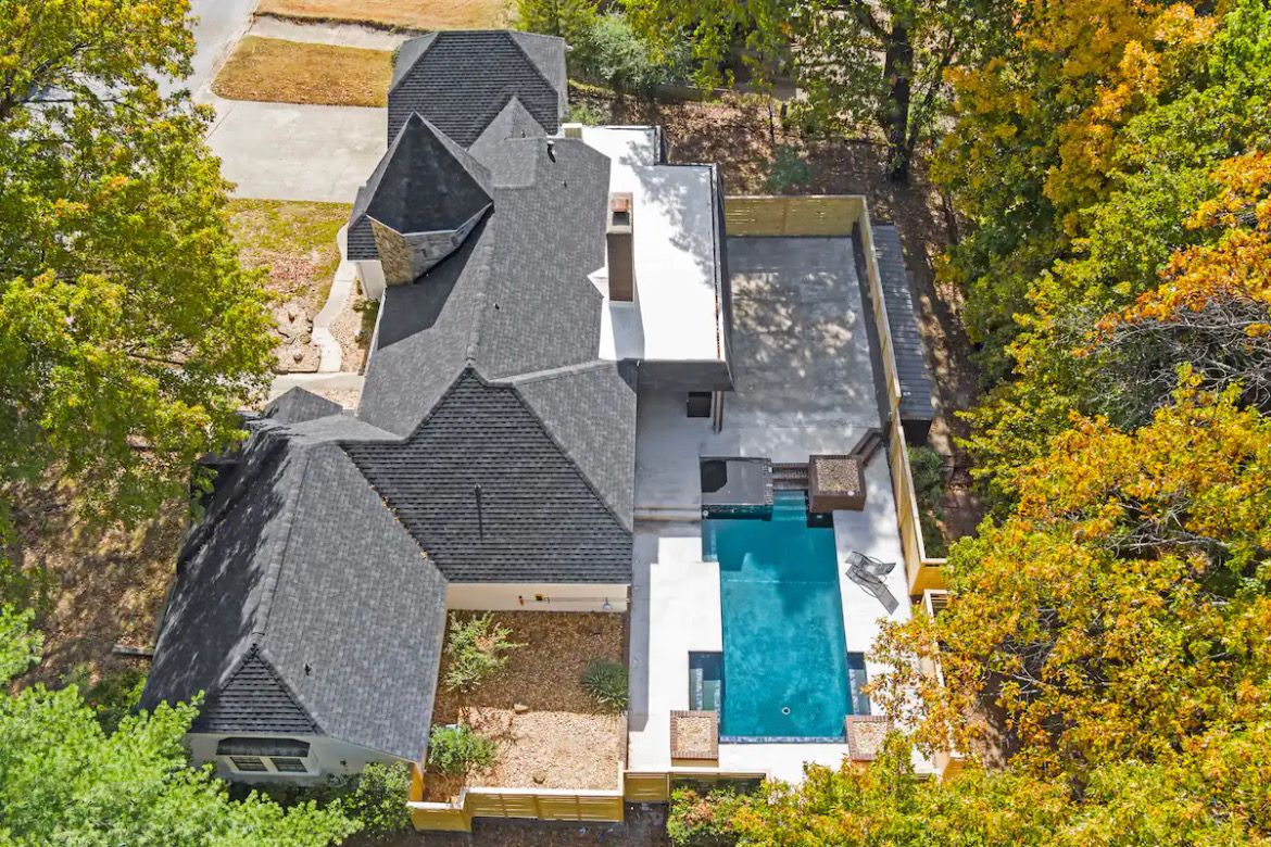 Uma casa com uma piscina grande, cercada por árvores e um gramado bem cuidado.