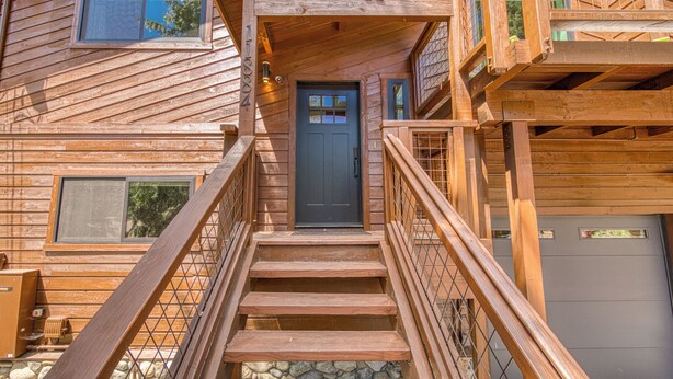 A wooden cabin with a front door, a staircase, and a garage.