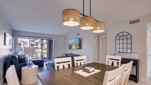 A modern dining area with a wooden table, white chairs, and a large window offering a view of buildings outside.