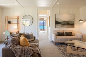 A modern living room with a sofa, a coffee table, a desk with a lamp, a chair, a round mirror, and a painting.