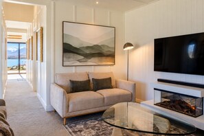 A living room with a beige sofa, a glass coffee table, a fireplace, a mounted TV, and a framed abstract painting.