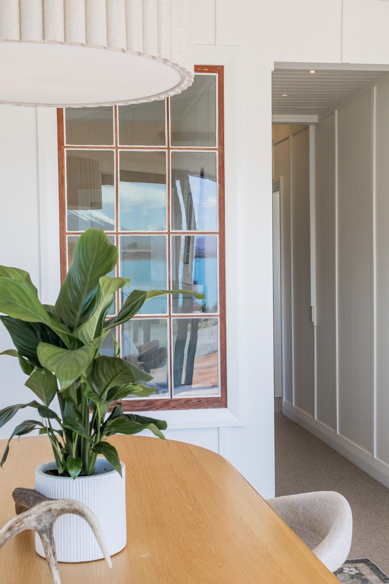 A room with a wooden table, a potted plant, and a window with a view of the outdoors.