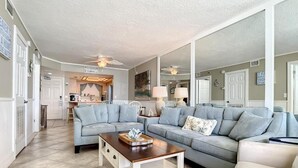 A spacious living room with a light blue sofa, a wooden coffee table, and a kitchen in the background.