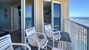 A balcony with white wicker chairs, a table, and a view of the ocean.