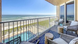 A balcony with a view of the ocean, outdoor furniture, and a pool.