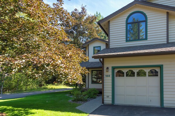 A two-story house with a garage, a well-maintained lawn, and a large tree with autumn leaves.