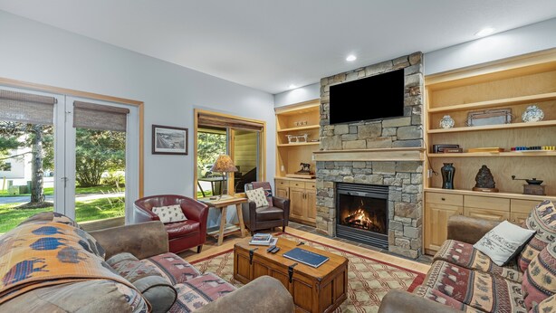 A cozy living room with a stone fireplace, comfortable seating, and a television mounted on the wall. - Mountain Harbor Hideaway! Walking distance to Whitefish Lake (Whitefish)