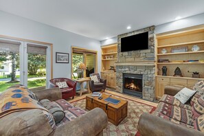 A cozy living room with a stone fireplace, comfortable seating, and a television mounted on the wall.